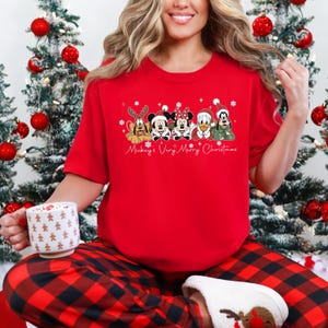 Puede incluir: Una camiseta roja de cuello redondo con un dise&ntilde;o navide&ntilde;o con personajes de Disney. El gr&aacute;fico incluye a Pluto, Mickey Mouse, Minnie Mouse, Donald Duck y Goofy. El texto "Mickey's Very Merry Christmas" est&aacute; escrito debajo.