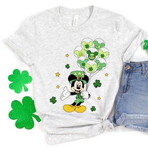 May include: A gray t-shirt with a green Mickey Mouse wearing a green hat and holding green balloons with shamrocks. The balloons have a green, white, and yellow color scheme.