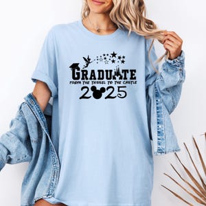 以下が含まれることがあります： 薄い青色のTシャツに、黒いグラフィックで「Graduate from the tassel to the castle 2025」と書いてあり、年の真ん中にミッキーマウスの頭があります。
