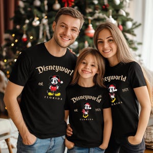 May include: A family of three wearing black t-shirts with a gold Mickey Mouse design. The shirts say "Disneyworld est. 1971 Florida".