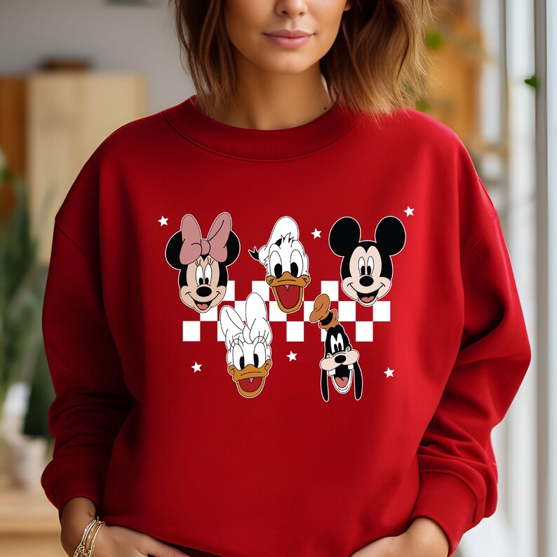 Puede incluir: Sudadera roja con un patr&oacute;n de cuadros blancos y un gr&aacute;fico de Mickey Mouse, Minnie Mouse, Donald Duck, Daisy Duck y Goofy. Los personajes sonr&iacute;en y tienen un fondo blanco.