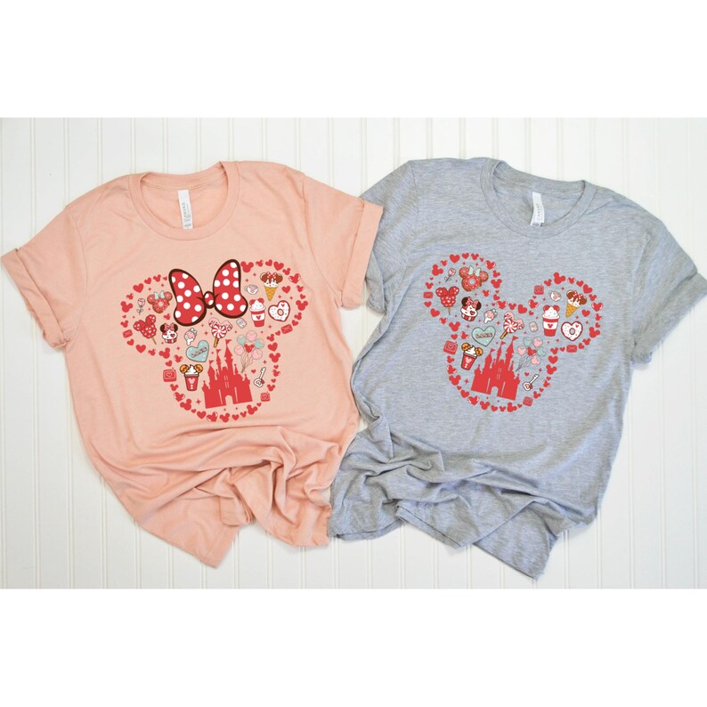 May include: Two t-shirts with a red and white Mickey Mouse head design. The design is made up of hearts and various Disney-themed icons, including the castle, Minnie Mouse, and a Mickey Mouse ice cream bar. One shirt is peach and the other is gray.