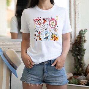 May include: White t-shirt with a colorful print of various Disney characters in frames. The characters include Mickey Mouse, Minnie Mouse, Pluto, and a pirate. The text "AUTUMN YORK ME" is printed on the shirt.