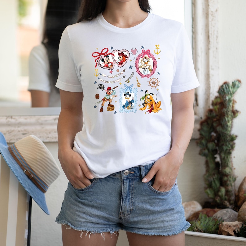 May include: White t-shirt with a colorful print of various Disney characters in frames. The characters include Mickey Mouse, Minnie Mouse, Pluto, and a pirate. The text "AUTUMN YORK ME" is printed on the shirt.