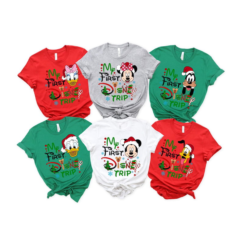 May include: Six red, green, and gray t-shirts with a Christmas theme. Each shirt features a different Disney character, including Mickey Mouse, Minnie Mouse, Donald Duck, Goofy, and Pluto. The shirts all have the text "My First Disney Trip" printed on them.