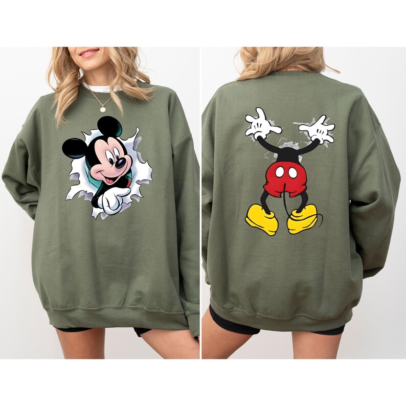 Puede incluir: Sudadera verde oliva con dise&ntilde;o de Mickey Mouse. La parte delantera muestra a Mickey rompiendo un agujero rasgado, mientras que la parte trasera muestra la pose ic&oacute;nica de Mickey. El dise&ntilde;o incluye detalles en negro, rojo, amarillo y blanco.