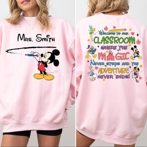May include: Pink sweatshirt with a Mickey Mouse design on the front and a Disney-themed quote on the back. The quote reads "Welcome to our classroom where the magic never stops and the adventure never ends!"