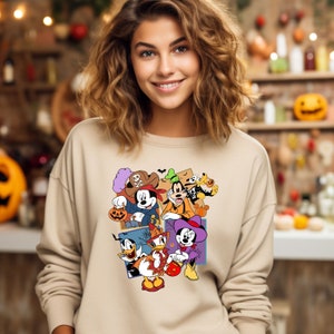 May include: A beige sweatshirt with a colorful graphic print of Mickey Mouse and his friends dressed in Halloween costumes. The characters are holding pumpkins and candy.