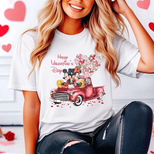 May include: White t-shirt with a graphic of Mickey and Minnie Mouse in a red pickup truck with pink heart balloons. The text "Happy Valentine's Day" is above the image.
