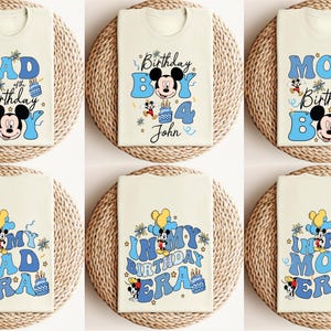 K&ouml;nnte beinhalten: Sechs wei&szlig;e T-Shirts mit blauen und gelben Mickey-Mouse-Geburtstagsdesigns. Die Shirts zeigen den Text "Papa des Geburtstagsknaben", "Mama des Geburtstagsknaben", "In My Dad Era", "In My Birthday Era" und "In My Mom Era". Ein Shirt hat den Text "Birthday Boy 4 John".