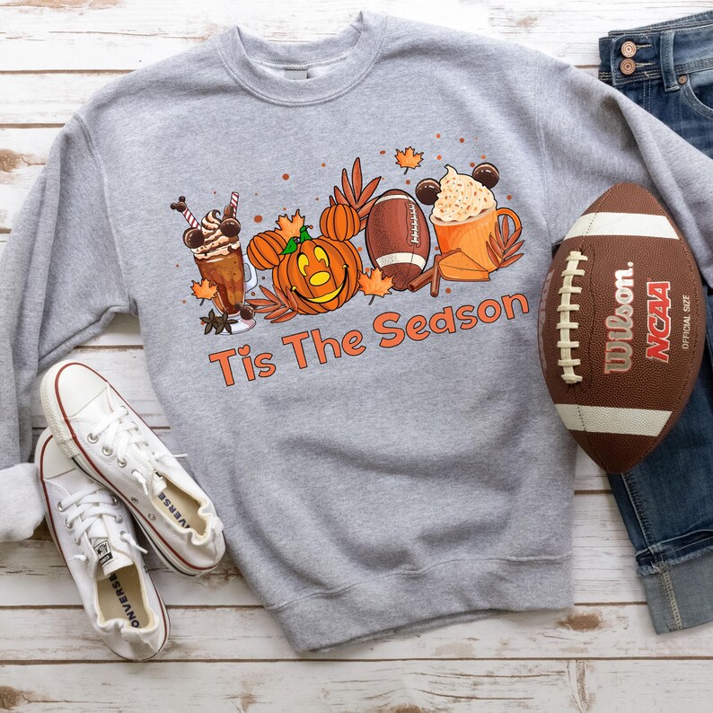 K&ouml;nnte beinhalten: Grauer Pullover mit einem Aufdruck von einem K&uuml;rbis, einem Football, einer Kaffeetasse und einem Milchshake mit dem Text "Tis The Season".