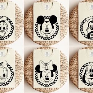 May include: Six white t-shirts with black and white chequered circles featuring different Disney characters: Donald Duck, Mickey Mouse, Goofy, Daisy Duck, Minnie Mouse, and Pluto.