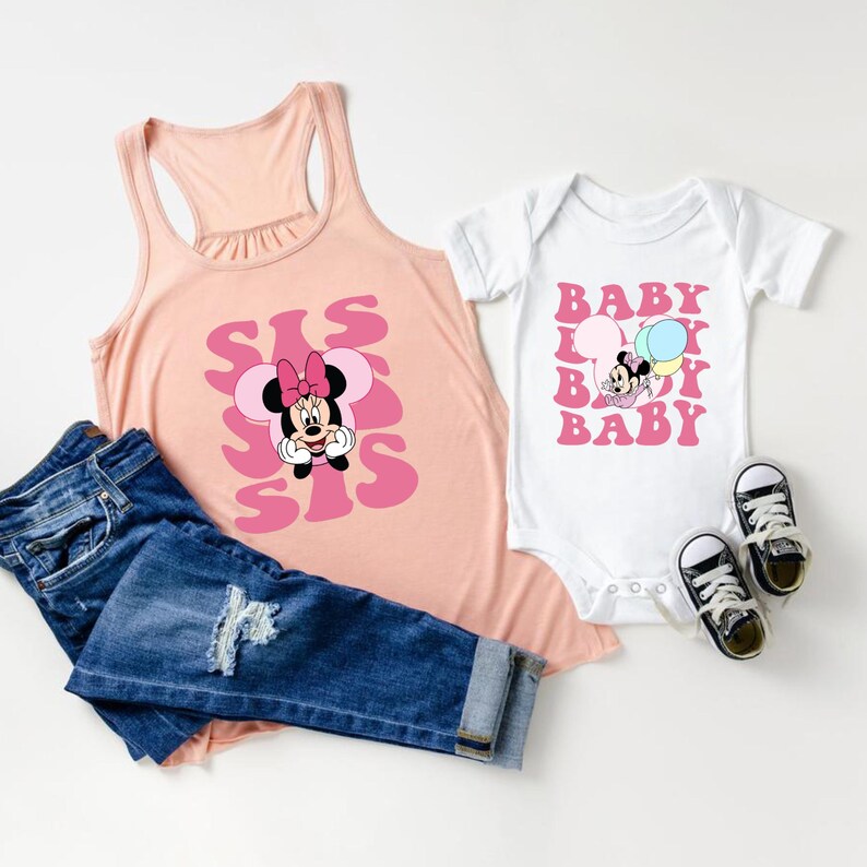 Puede incluir: Una camiseta sin mangas rosa claro con un gr&aacute;fico de Minnie Mouse y la palabra "SIS" repetida. Un body blanco para beb&eacute; con un gr&aacute;fico de Minnie Mouse y la palabra "BABY". Vaqueros azules y dos pares de zapatillas blancas y negras completan el conjunto.