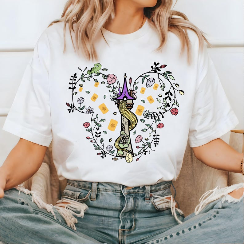 May include: White t-shirt with a floral design featuring a purple tower with a long blonde braid, surrounded by yellow lanterns and green leaves.