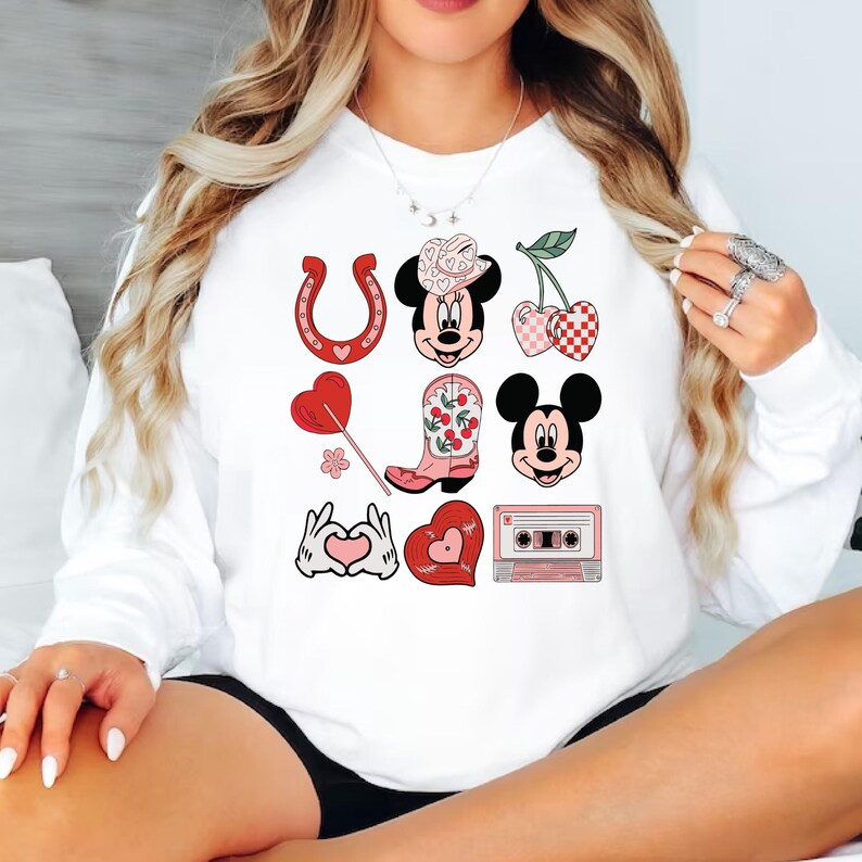 May include: White sweatshirt with a red, pink and white graphic design featuring Mickey Mouse, a horseshoe, a cowboy boot, cherries, a heart and a cassette tape.