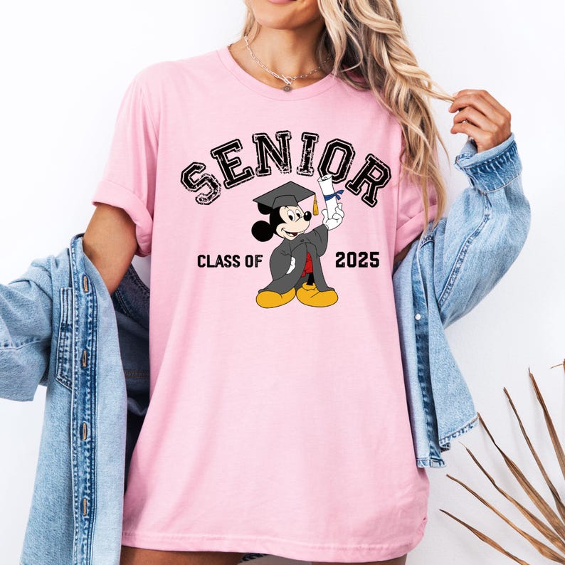 K&ouml;nnte beinhalten: Rosafarbenes T-Shirt mit einem schwarzen Aufdruck von Mickey Mouse, der einen Abschluss-Hut tr&auml;gt und ein Diplom h&auml;lt. Der Text "Senior Class of 2025" ist auf dem T-Shirt aufgedruckt.