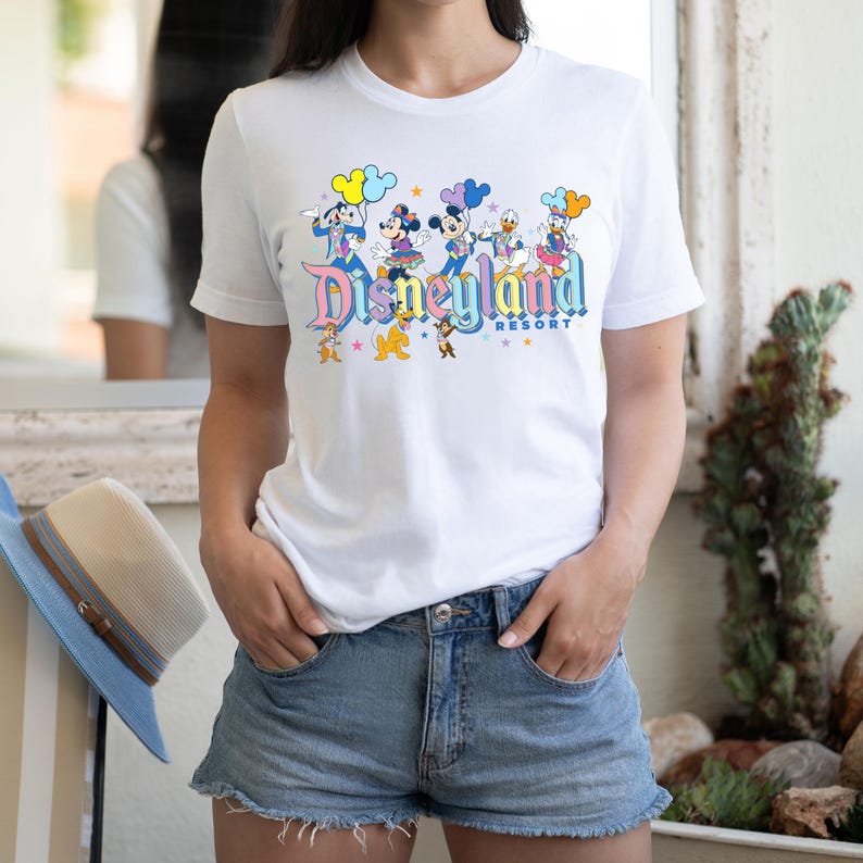 May include: White t-shirt featuring a colourful graphic of Mickey Mouse and his friends in front of the Disneyland Resort logo.