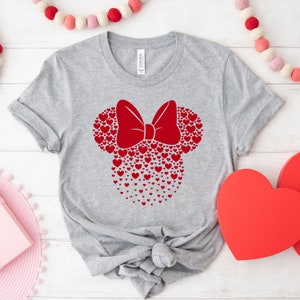 May include: A gray t-shirt with a red heart design in the shape of Mickey Mouse ears with a bow. The design is made up of small red hearts.