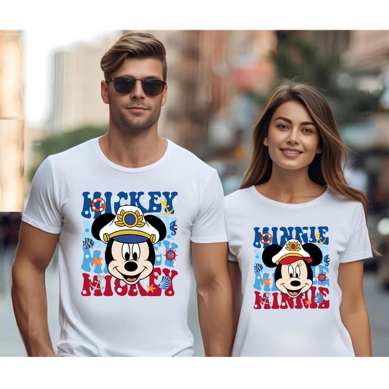 May include: White t-shirts with a nautical themed Mickey Mouse and Minnie Mouse design. Mickey Mouse is wearing a captain's hat and Minnie Mouse is wearing a captain's hat with a red bow. The shirts have the text "Mickey Mickey" and "Minnie Minnie" on them.