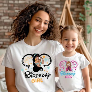 May include: Two white t-shirts with a Disney princess theme. The larger shirt features Jasmine from Aladdin with the text "Birthday Girl". The smaller shirt features Elsa from Frozen with the text "Birthday Girl".