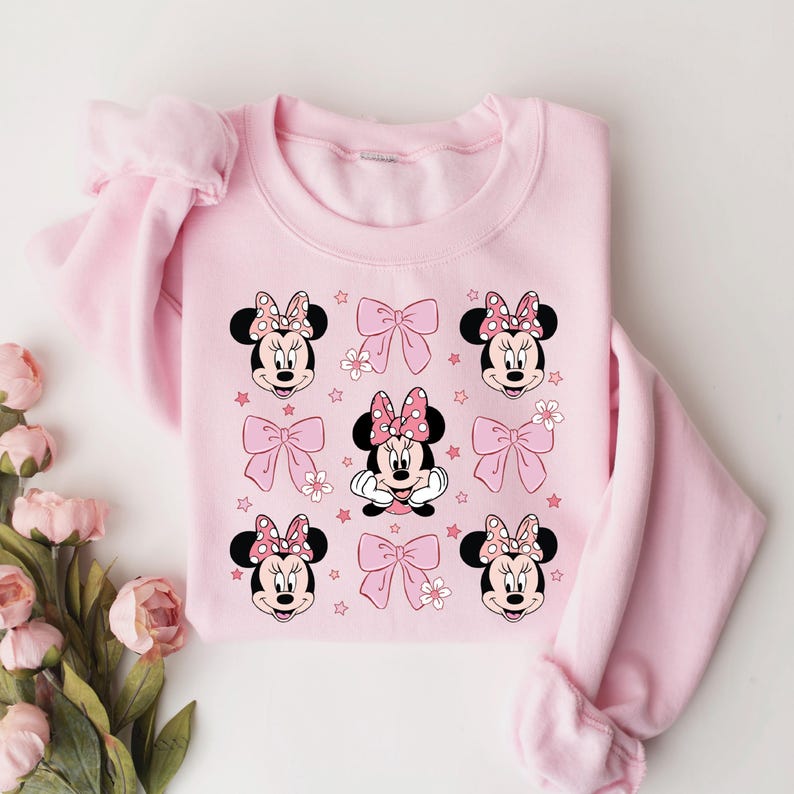 May include: Pink sweatshirt with a graphic print of Minnie Mouse. The print features multiple images of Minnie Mouse with pink bows and stars.