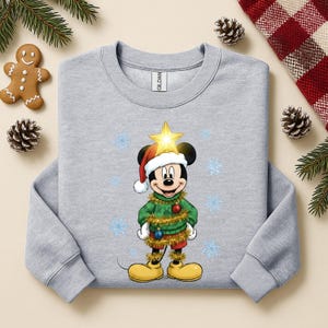 Pode incluir: Um moletom cinza claro com um design do Mickey Mouse com tema natalino. Mickey est&aacute; vestido como uma &aacute;rvore de Natal, usando um gorro de Papai Noel e uma estrela. O design inclui flocos de neve e decora&ccedil;&otilde;es festivas.