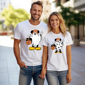 May include: White t-shirts featuring a Halloween-themed cartoon character dressed as a ghost, holding a jack-o'-lantern. The character has black ears, an orange hat, and yellow shoes. The design is on a white t-shirt.