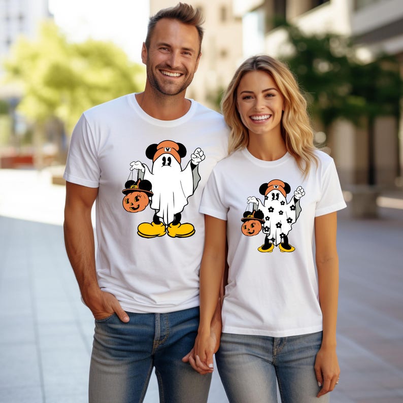 May include: White t-shirts featuring a Halloween-themed cartoon character dressed as a ghost, holding a jack-o'-lantern. The character has black ears, an orange hat, and yellow shoes. The design is on a white t-shirt.