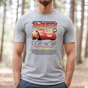 May include: A gray t-shirt featuring Lightning McQueen, a red race car from the Cars movie. The shirt includes the text "LIGHTNING MCQUEEN" and "95", along with the phrase "I'm faster than fast. Quicker than quick."