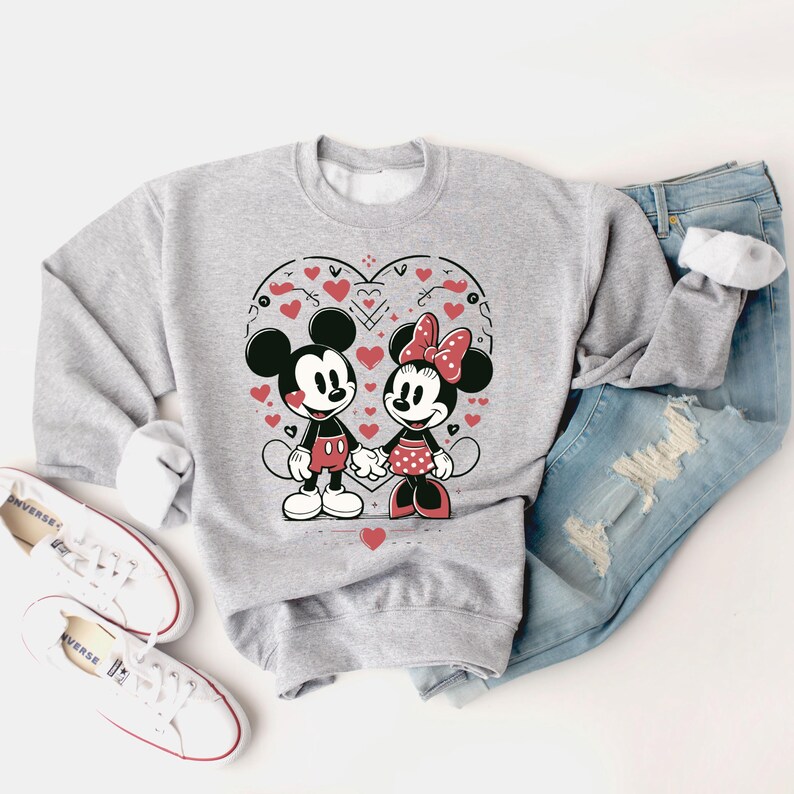 May include: A gray sweatshirt with a graphic print of Mickey Mouse and Minnie Mouse holding hands. The graphic is surrounded by red hearts and a heart-shaped outline.