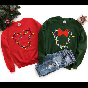 May include: Two Christmas themed sweatshirts, one red and one green, with a Mickey Mouse and Minnie Mouse design made of colorful Christmas lights.
