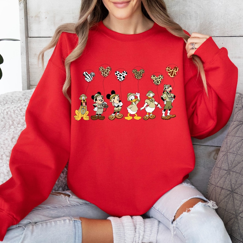 Pode incluir: Camisola vermelha com um gr&aacute;fico de Mickey Mouse, Donald Duck, Pateta e Pluto vestindo roupas de saf&aacute;ri e segurando bal&otilde;es com desenhos de estampas de animais.