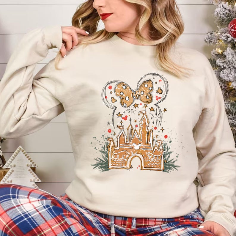 K&ouml;nnte beinhalten: Cremefarbenes Sweatshirt mit Lebkuchenschloss und Minnie-Mouse-Schleifendesign. Die Grafik enth&auml;lt Sterne, Feuerwerk und festliche Akzente. Das Sweatshirt ist ein gem&uuml;tliches Oberteil mit langen &Auml;rmeln.