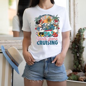 May include: White t-shirt with a colorful graphic of Mickey Mouse and Minnie Mouse on a boat with the text "Girls gone cruising".