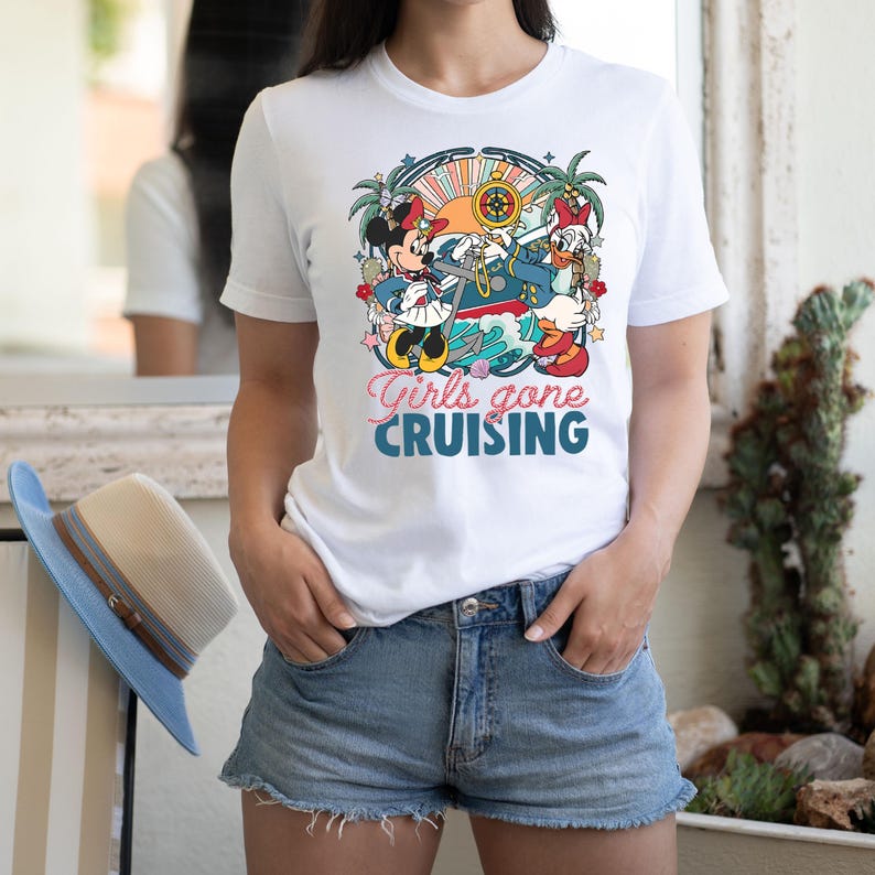May include: White t-shirt with a colorful graphic of Mickey Mouse and Minnie Mouse on a boat with the text "Girls gone cruising".