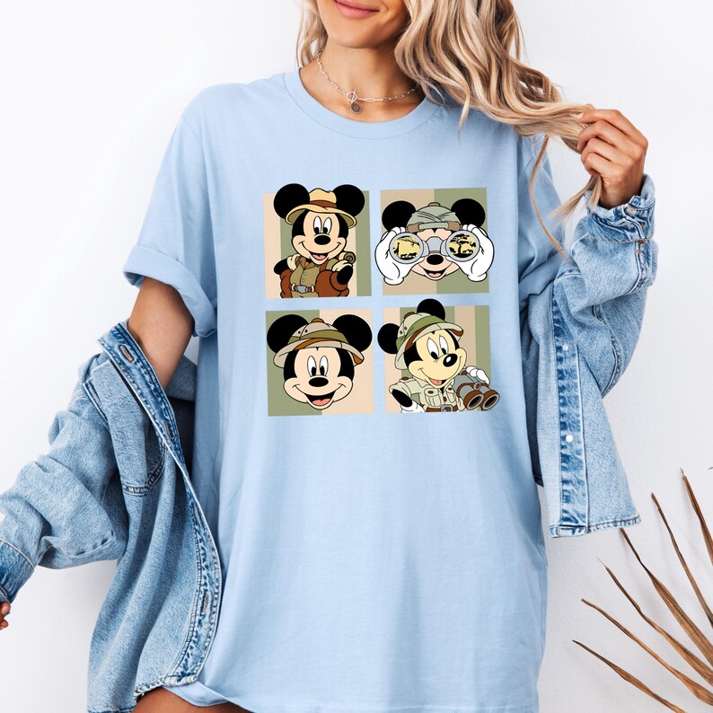 K&ouml;nnte beinhalten: Hellblaues T-Shirt mit vier Feldern, die Micky Maus in Safari-Kleidung zeigen. Jedes Feld zeigt Micky in verschiedenen Posen, mit Safarihut und Fernglas. Der Hintergrund jedes Feldes ist eine Mischung aus Beige, Gr&uuml;n und Olivgr&uuml;n.