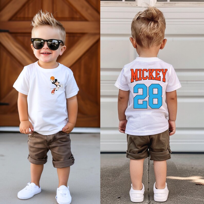 May include: A white t-shirt with a Mickey Mouse basketball graphic on the front and the text "Mickey 28" on the back. The shirt is being worn by a young boy with brown hair and sunglasses. He is wearing brown shorts and white sneakers.