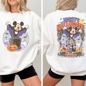 May include: White sweatshirt featuring a Mickey Mouse Halloween design. Mickey is dressed as a vampire and the text reads "Mickey's Halloween" and "Candy Co."