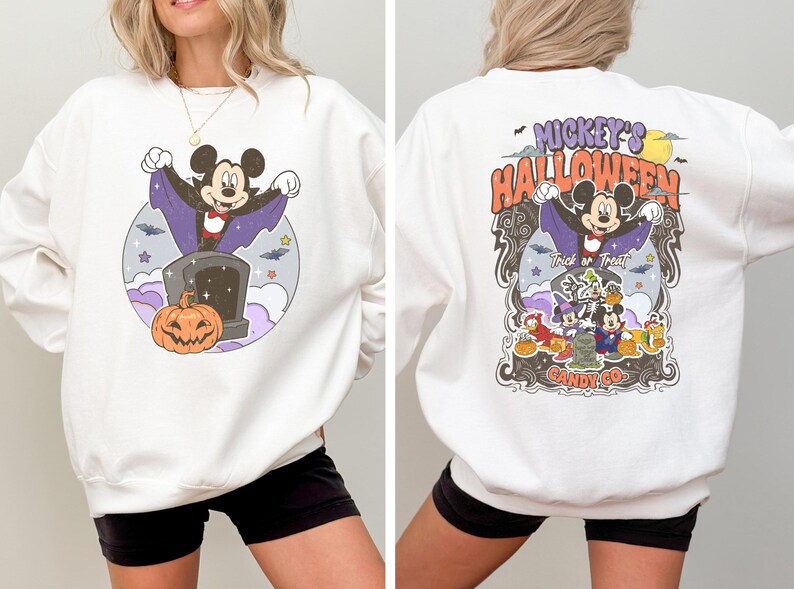 May include: White sweatshirt featuring a Mickey Mouse Halloween design. Mickey is dressed as a vampire and the text reads "Mickey's Halloween" and "Candy Co."