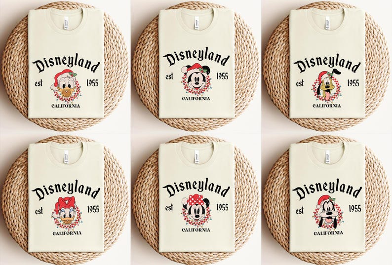 May include: Six cream-colored t-shirts with a Christmas-themed Disneyland logo featuring different Disney characters. The logo reads "Disneyland est 1955 California".