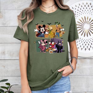 Puede incluir: Camiseta verde oliva con un dise&ntilde;o de Halloween con personajes de dibujos animados. El dise&ntilde;o incluye a Mickey Mouse, Minnie Mouse, Donald Duck, Goofy y otros personajes con disfraces de Halloween, con murci&eacute;lagos negros.