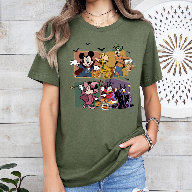 Puede incluir: Camiseta verde oliva con un dise&ntilde;o de Halloween con personajes de dibujos animados. El dise&ntilde;o incluye a Mickey Mouse, Minnie Mouse, Donald Duck, Goofy y otros personajes con disfraces de Halloween, con murci&eacute;lagos negros.