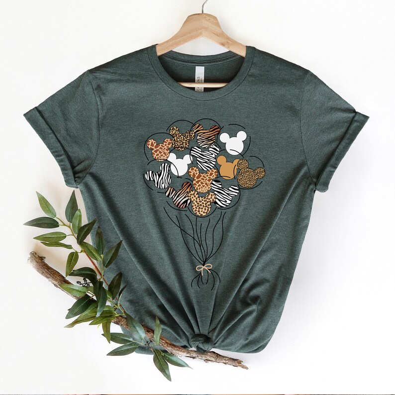 Puede incluir: Una camiseta verde con un gr&aacute;fico de cabezas de Mickey Mouse en forma de globos. Los globos est&aacute;n impresos con patrones de estampado animal, incluyendo cebra, leopardo y jirafa.