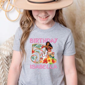 以下が含まれることがあります： 5歳の誕生日を祝う、カラフルなグラフィックデザインのグレーのTシャツ。「BIRTHDAY」の文字と、大きな数字の「5」、花の装飾、漫画のキャラクター、そして名前の「ISABELLA」が描かれています。