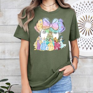May include: A green t-shirt with a colorful graphic of Disney princesses in front of Cinderella's castle. The graphic includes a large pink bow with white polka dots.