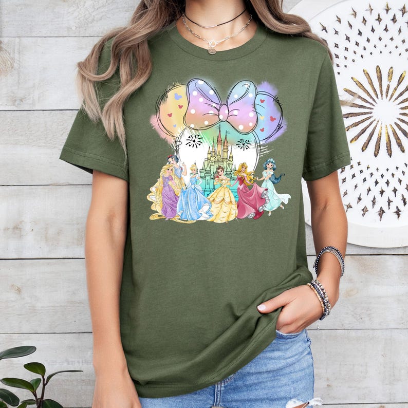 May include: A green t-shirt with a colorful graphic of Disney princesses in front of Cinderella's castle. The graphic includes a large pink bow with white polka dots.