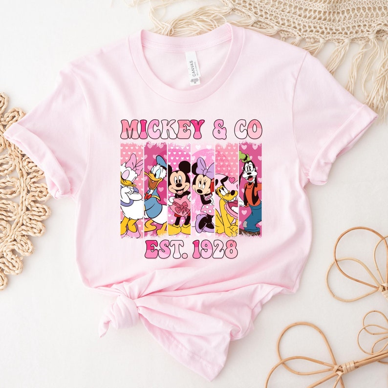 Puede incluir: Camiseta rosa con un gr&aacute;fico de Mickey Mouse y sus amigos en un dise&ntilde;o a rayas rosa y blanco. El texto "Mickey & Co. Est. 1928" est&aacute; impreso en la camiseta.