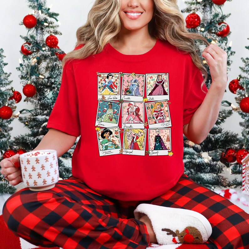 Puede incluir: Camiseta roja con una cuadr&iacute;cula de nueve retratos de princesas al estilo polaroid. Las princesas visten diferentes atuendos y posan. La persona lleva un pantal&oacute;n de pijama a cuadros rojos y negros y sostiene una taza con hombres de jengibre.