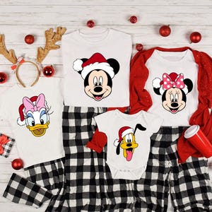 May include: A set of four Christmas pajamas featuring Mickey Mouse, Minnie Mouse, Donald Duck, and Pluto. The pajamas are white with red and black plaid accents. Each pajama top features a different character wearing a Santa hat.