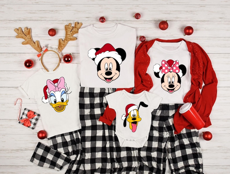 May include: A set of four Christmas pajamas featuring Mickey Mouse, Minnie Mouse, Donald Duck, and Pluto. The pajamas are white with red and black plaid accents. Each pajama top features a different character wearing a Santa hat.